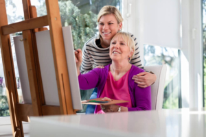 Caregiver supporting client as she paints a picture