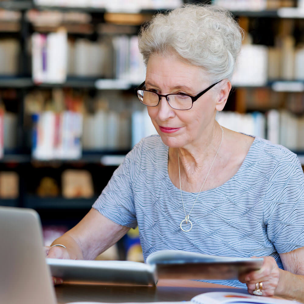 Older woman doing research in a library and online